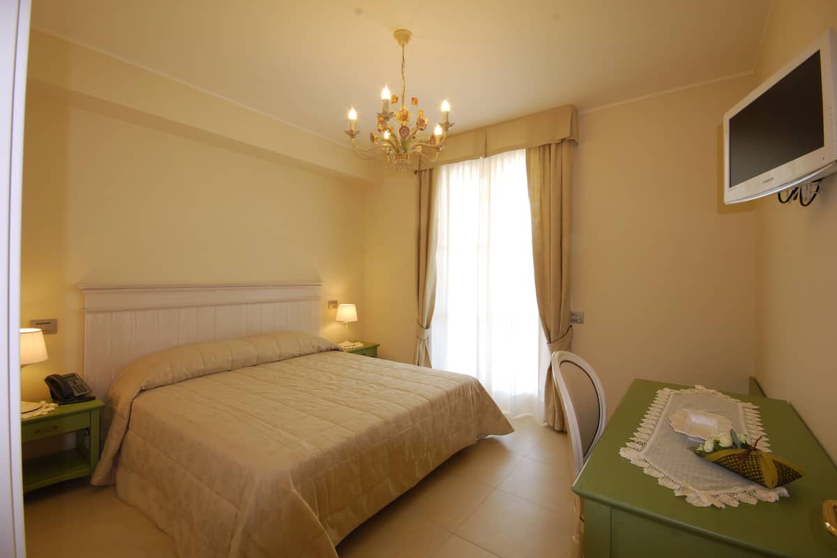 A hotel room with a large bed, a desk with a television, and a chandelier.