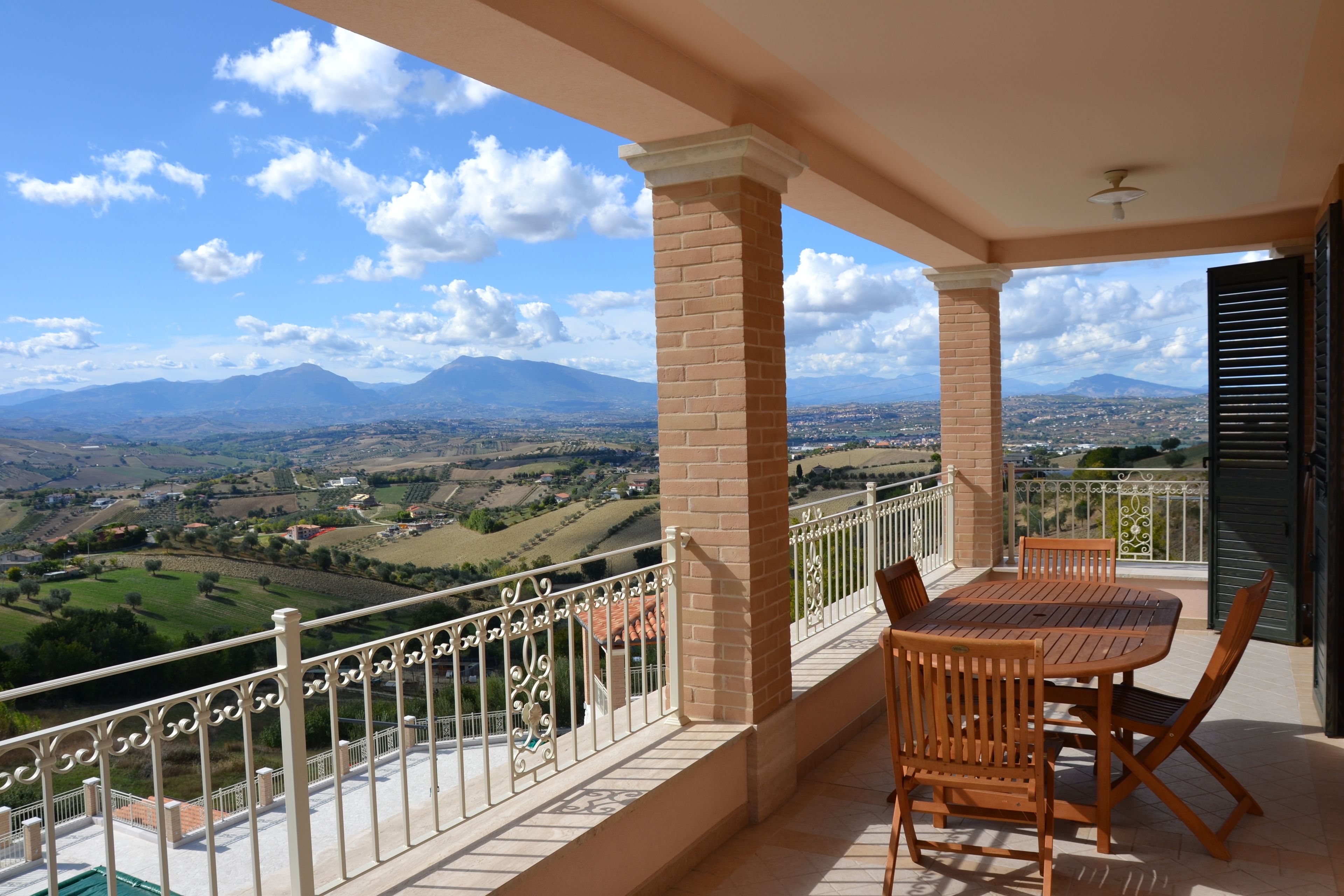 A balcony with a table and chairs, offering a view of a mountainous landscape.