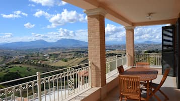 A balcony with a table and chairs, offering a view of a mountainous landscape.