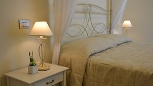 Una cama bien hecha con un edredón color beige, una mesita de noche con una lámpara y una pequeña planta en maceta.