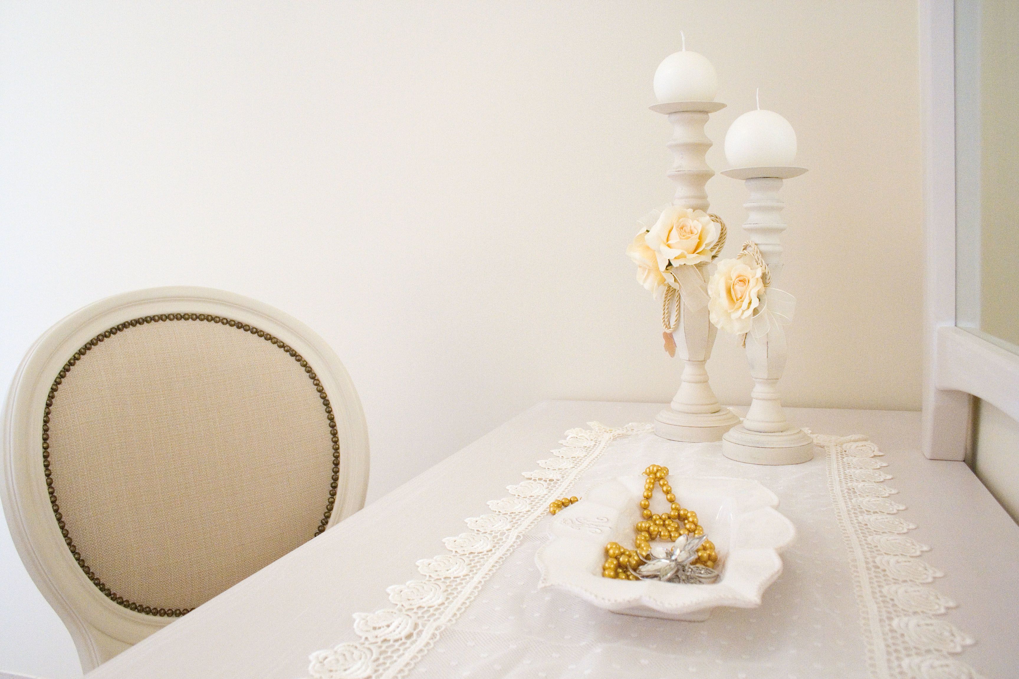 Une table recouverte d’une nappe en dentelle, un chandelier blanc orné de fleurs et un bol rempli de perles dorées et argentées.