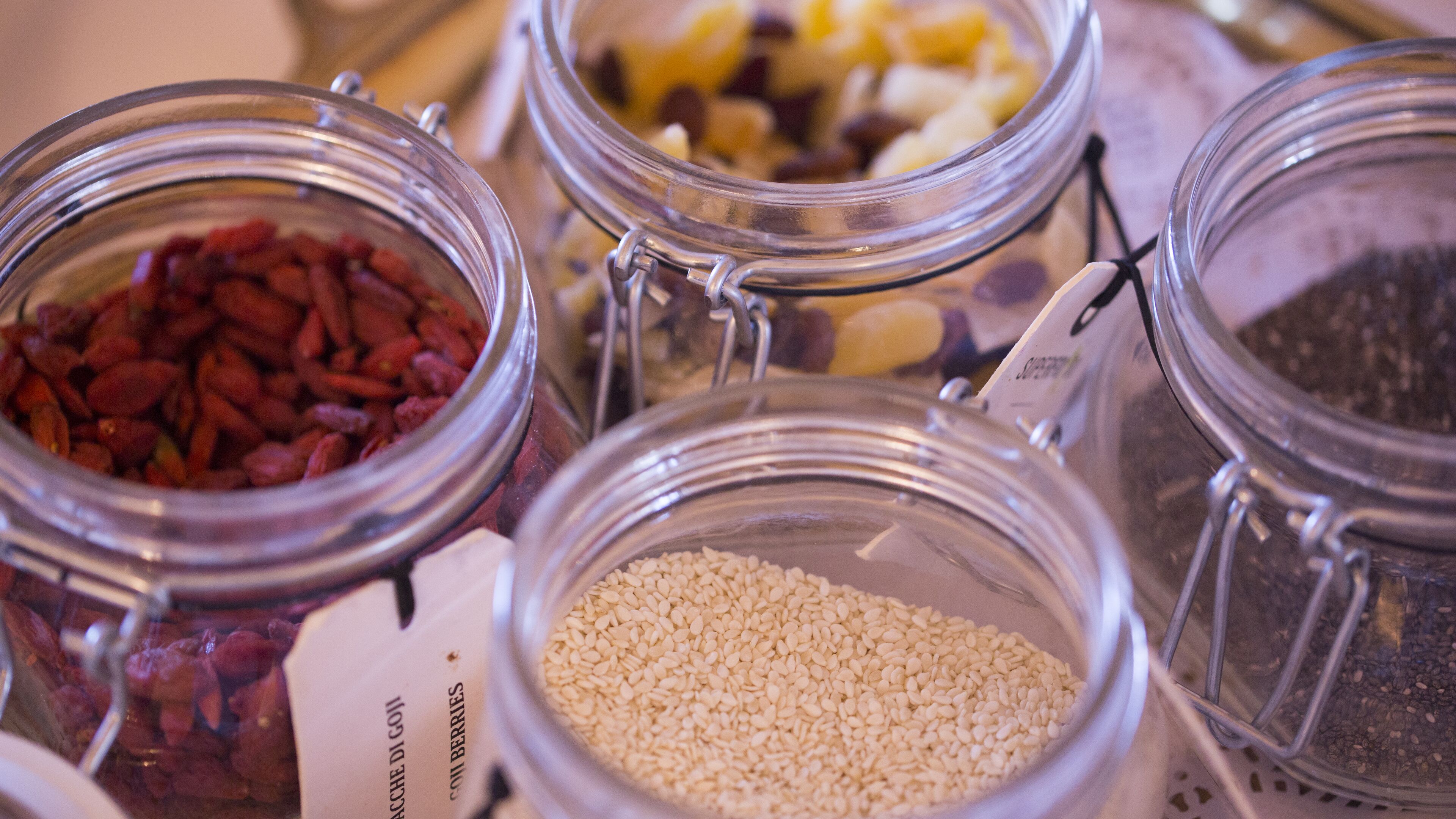 A close-up of several glass jars containing different types of seeds and dried fruits.