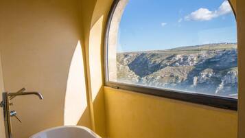 A bathroom with a bathtub, a window with a view of a mountainous landscape, and a shower area.