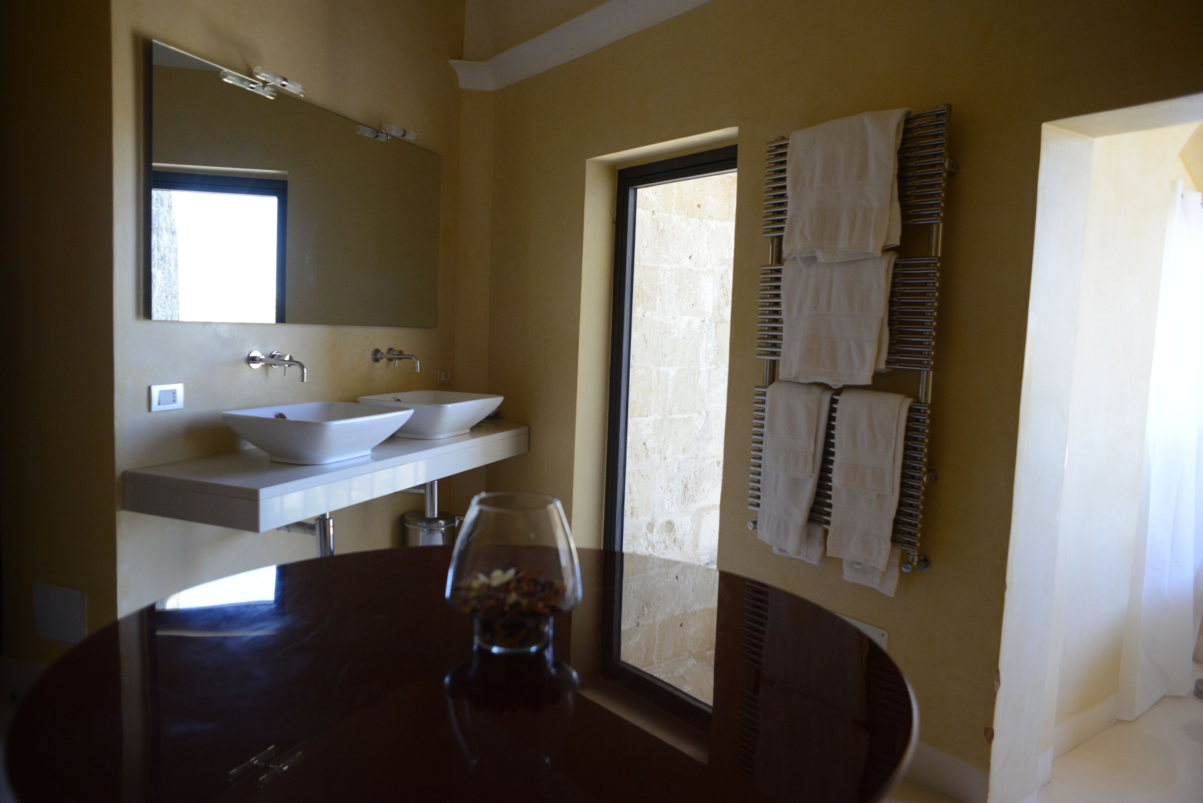 A bathroom with two sinks, a large mirror, and a round table with a glass and a bottle.