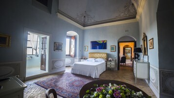 Um quarto espaçoso com uma cama grande, um espaço de estar com mesa e cadeiras, e vista para o corredor.