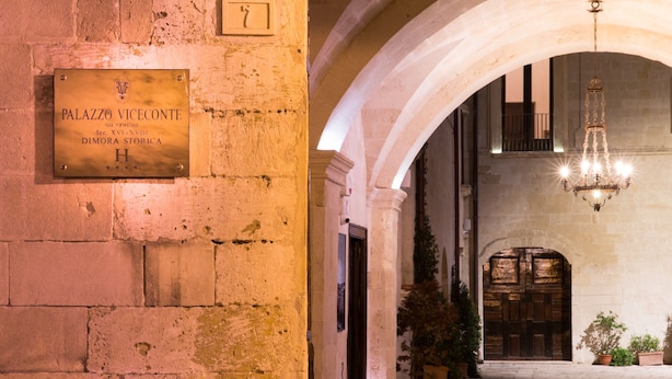 A historic building with a plaque reading "PALAZZO VICEONTI" and an arched corridor with a chandelier.