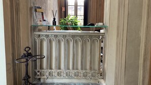 A hallway with a stone floor, a decorative radiator, a glass shelf with books and a plant, and a window with natural light. - Castello La Rocchetta (Sandigliano)