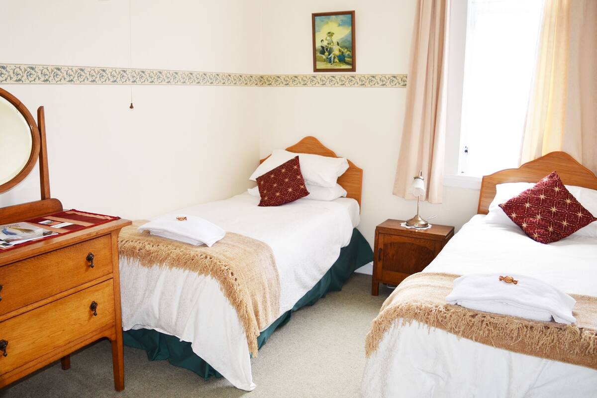 Une chambre d’hôtel avec deux lits, une commode en bois, un miroir et un tableau au mur.