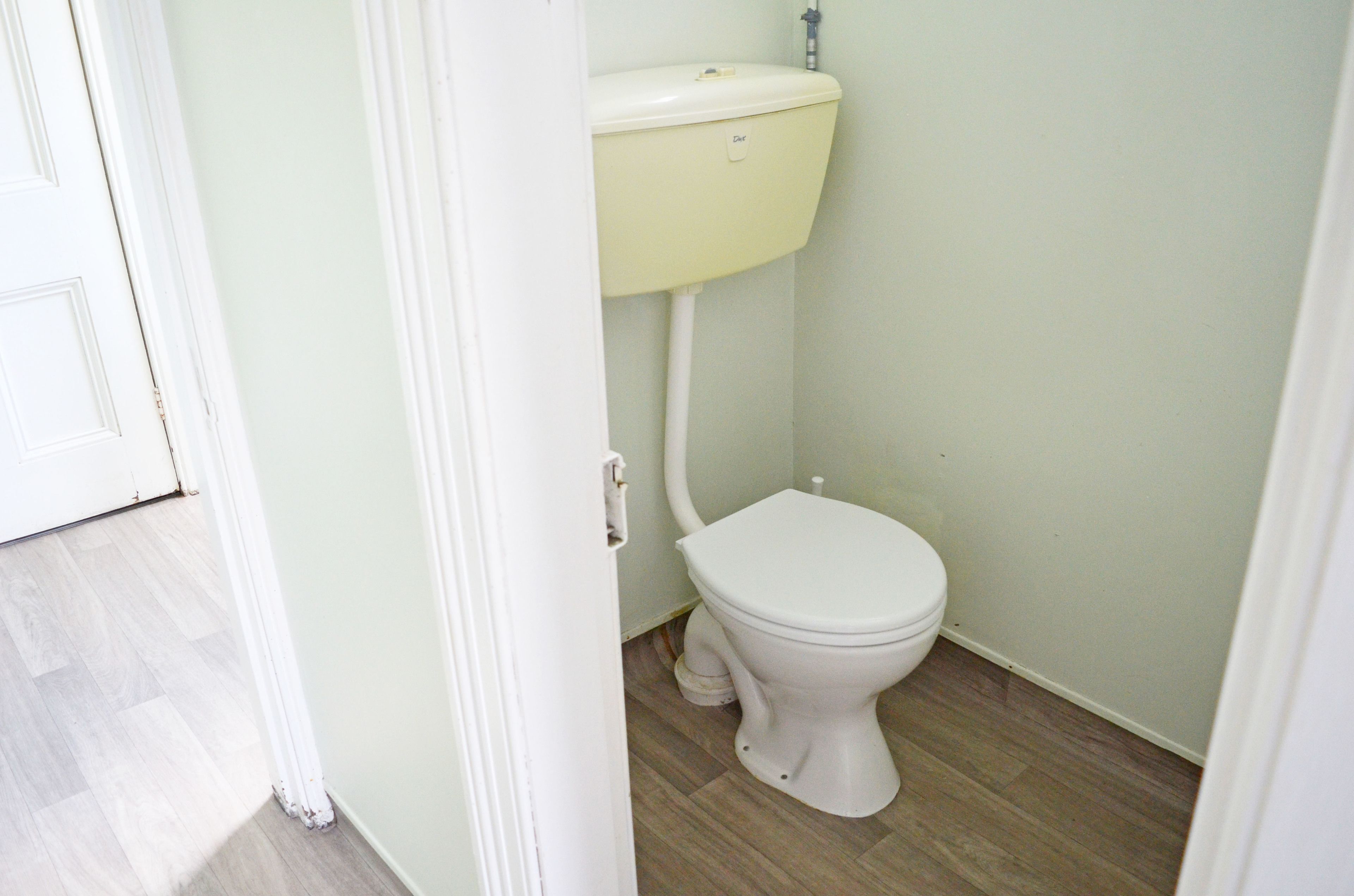 A small, clean bathroom with a white toilet and a light green wall.