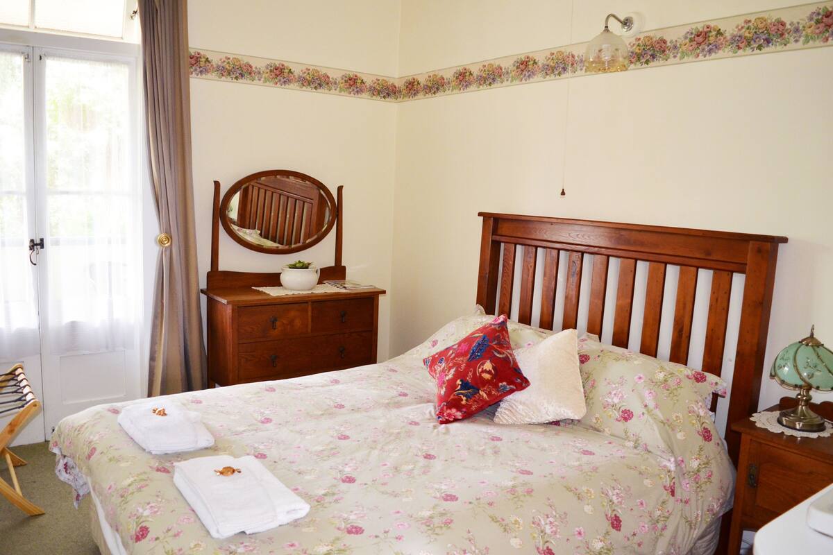 Un lit bien fait, avec une literie à motifs floraux, une tête de lit en bois et une table de chevet sur laquelle se trouve une lampe.