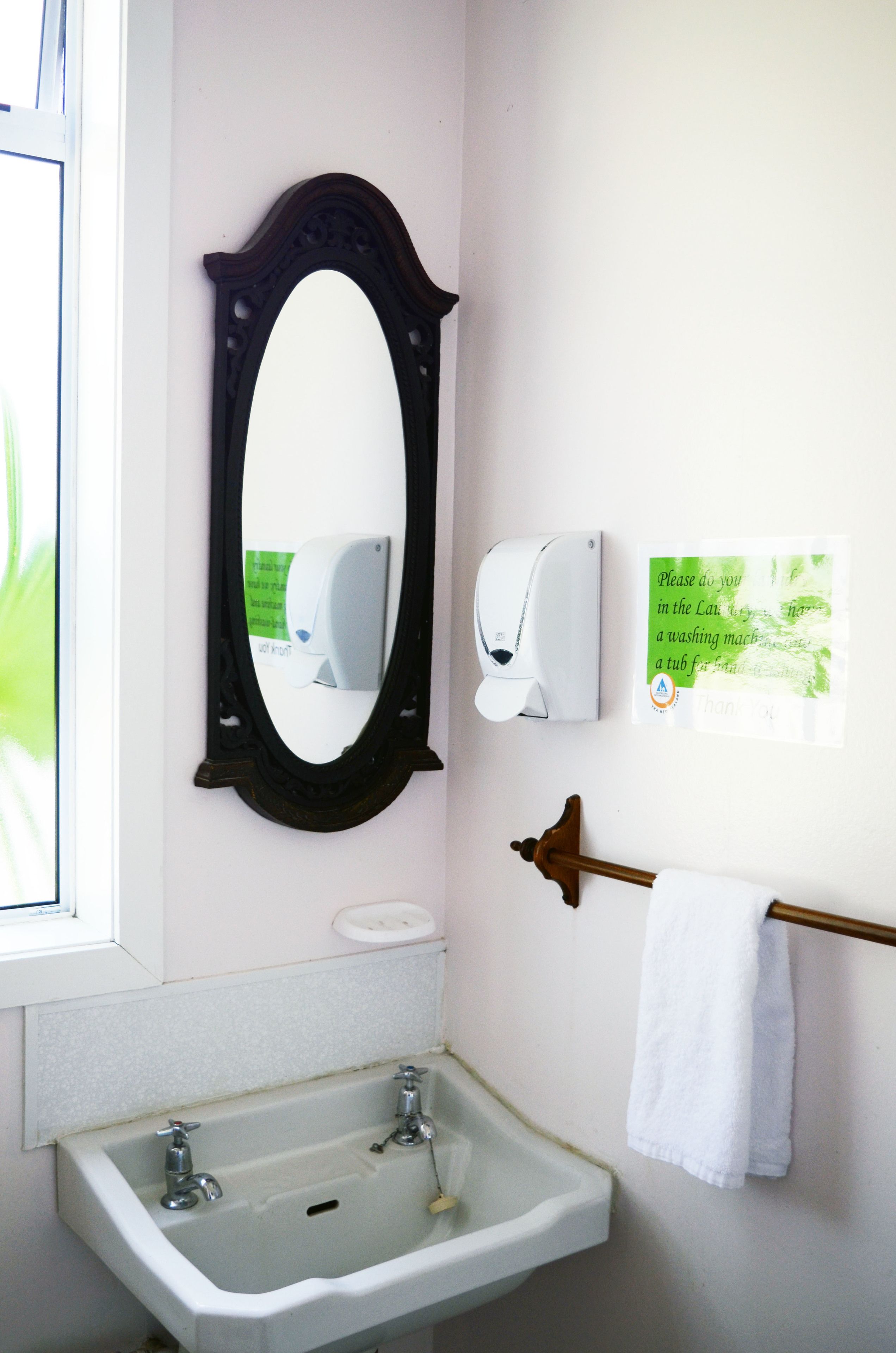 Un baño con un lavabo blanco, un espejo, dispensador de jabón y un perchero para toallas.