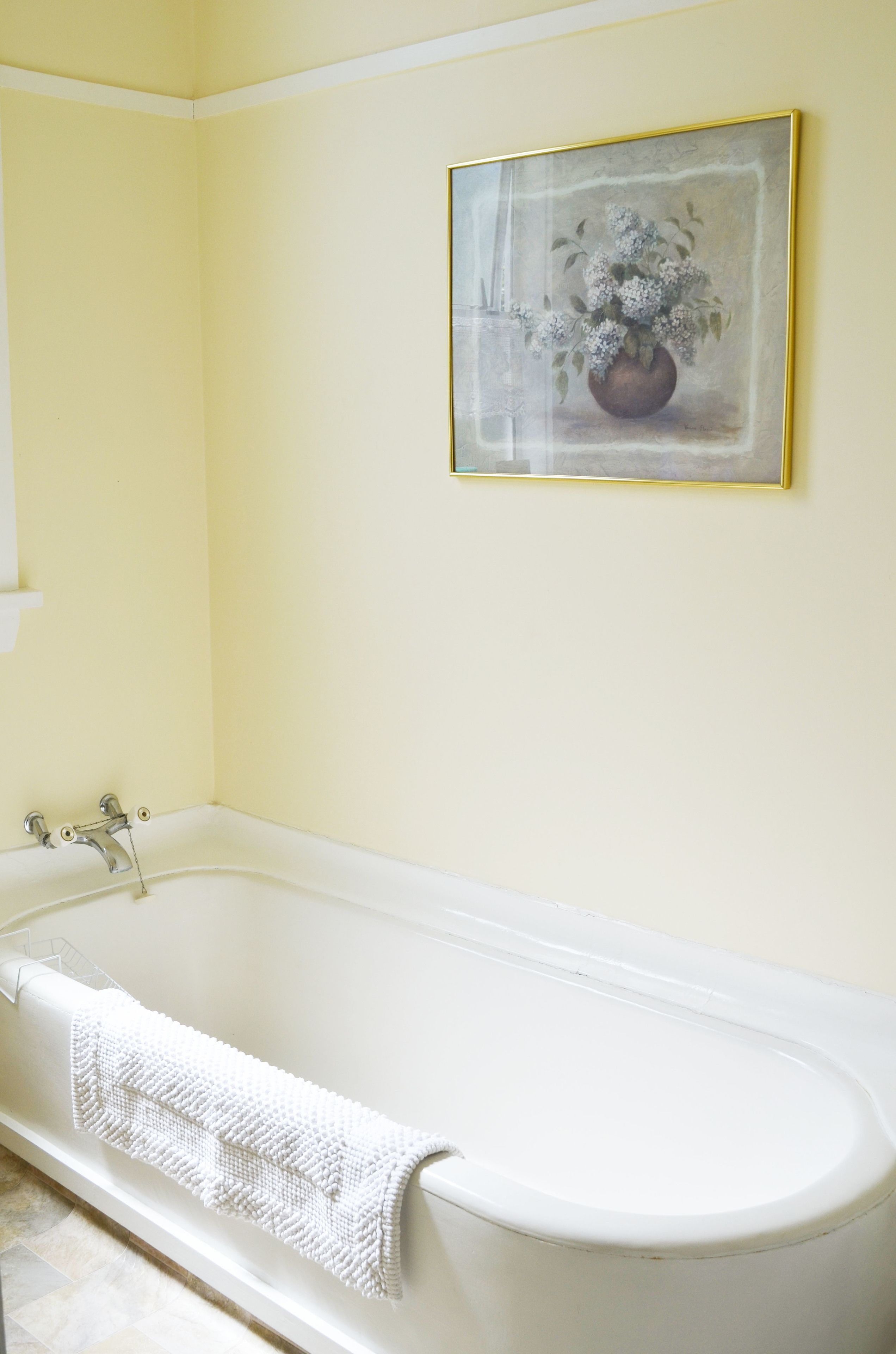 A bathroom with a white bathtub, a white towel, and a framed painting on the wall.