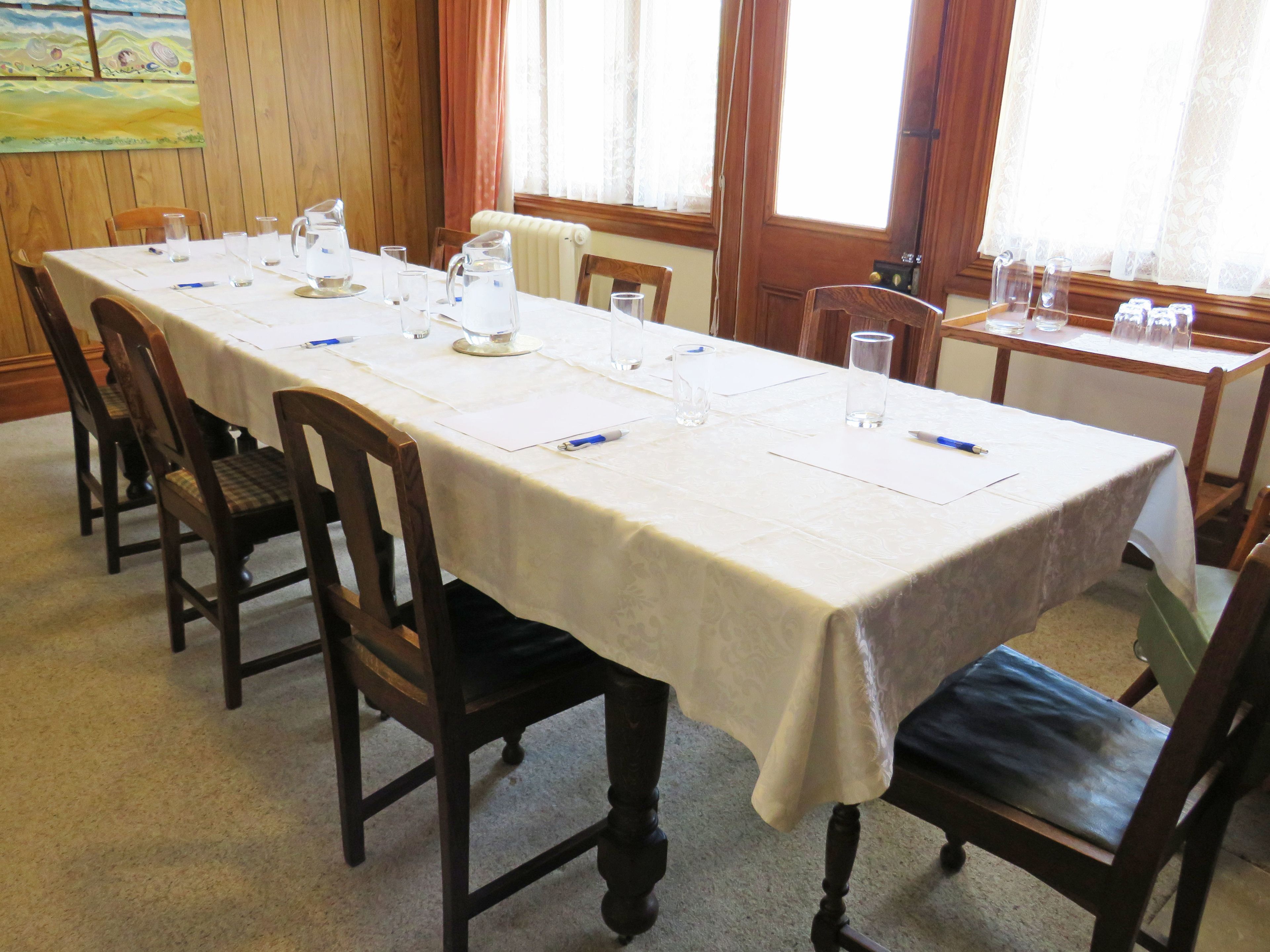 A conference room with a long table, chairs, and various items like water pitchers and pens.