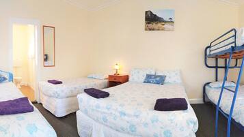 Quarto com três camas de solteiro, uma cama beliche, uma mesa de cabeceira com luminária, um espelho e um quadro na parede.