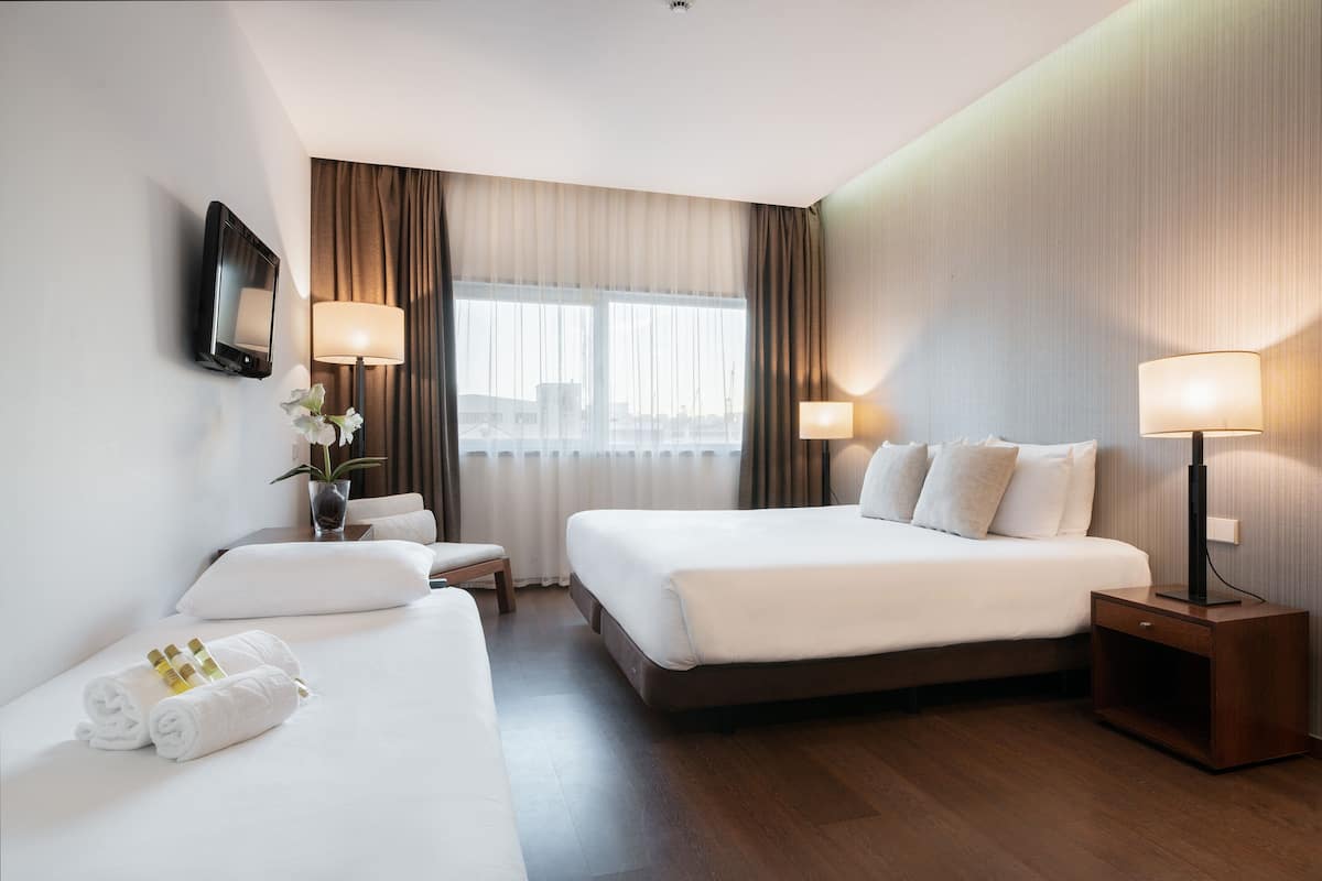 A hotel room with two beds, a TV, a desk, and a lamp.