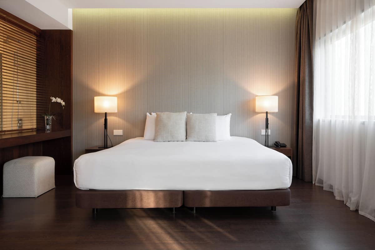 A large bed with two bedside lamps, a wooden bench, and a wall with vertical lines.