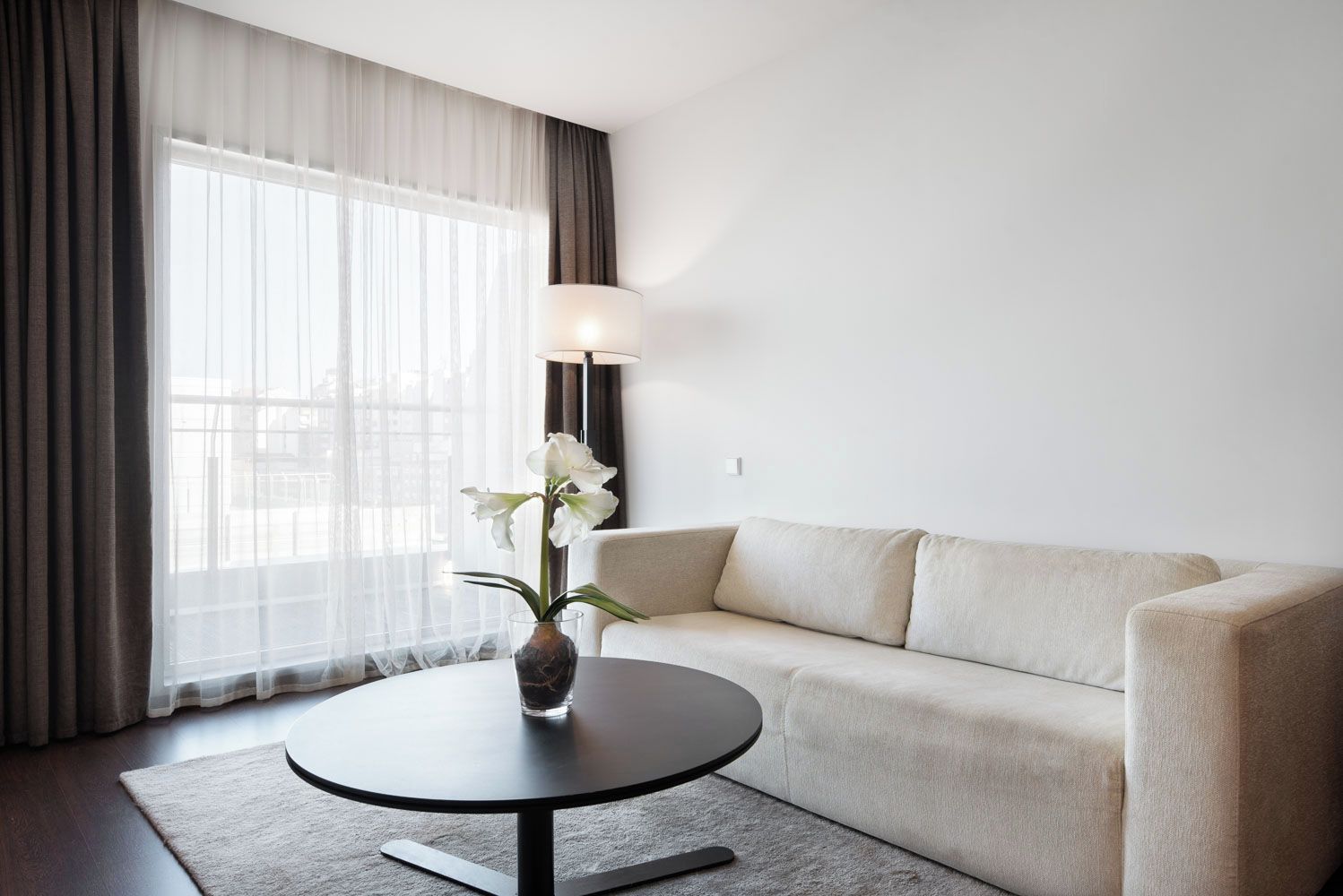 A modern living room with a sofa, a round coffee table, a vase with flowers, and a lamp.