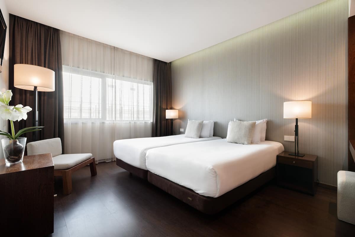 A hotel room with a large bed, two bedside tables, a chair, a desk, and a window with curtains.