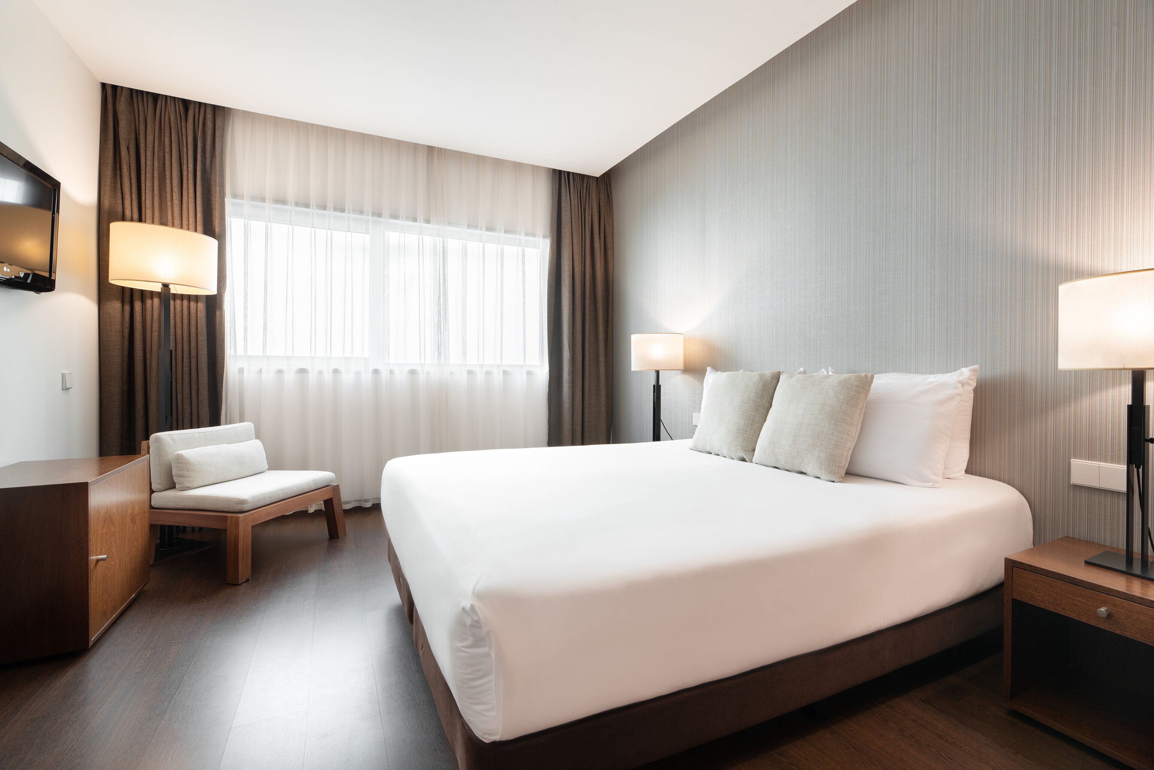 A modern hotel room with a large bed, a seating area, and a TV.