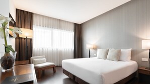 A hotel room with a large bed, a desk with a lamp, a chair, and a vase with flowers. - Eurostars Mar de Vigo (Vigo)