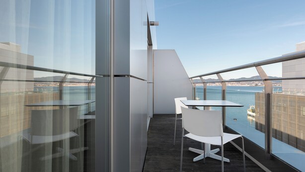 A balcony with a table and chairs, overlooking a body of water and distant cityscape. - Eurostars Mar de Vigo (Vigo)