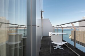 Un balcón con mesa y sillas, con vistas a un cuerpo de agua y un paisaje urbano distante.
