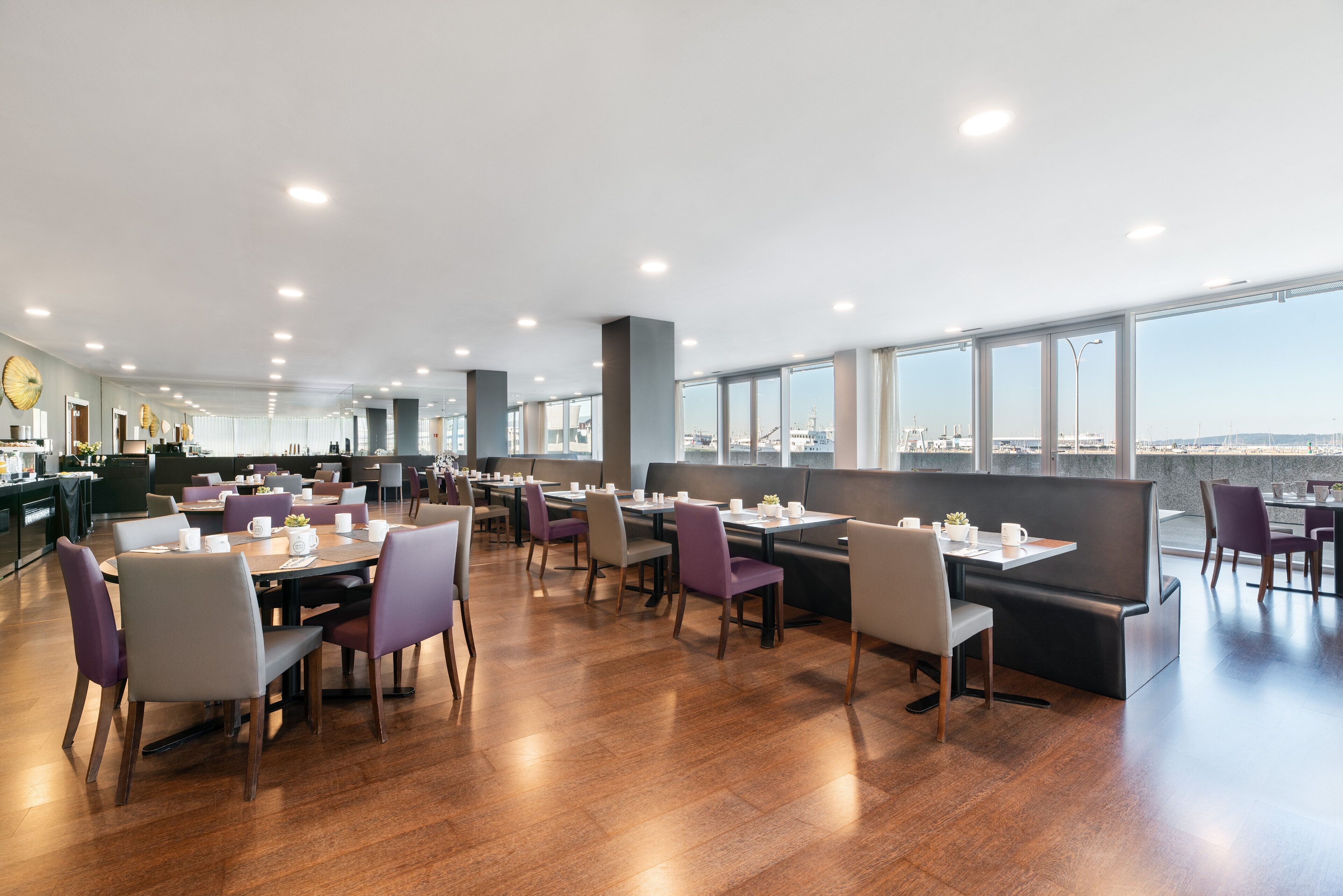 Un restaurant spacieux doté de plusieurs espaces de restauration, de grandes fenêtres offrant une vue sur la ville et d’un aménagement intérieur moderne.