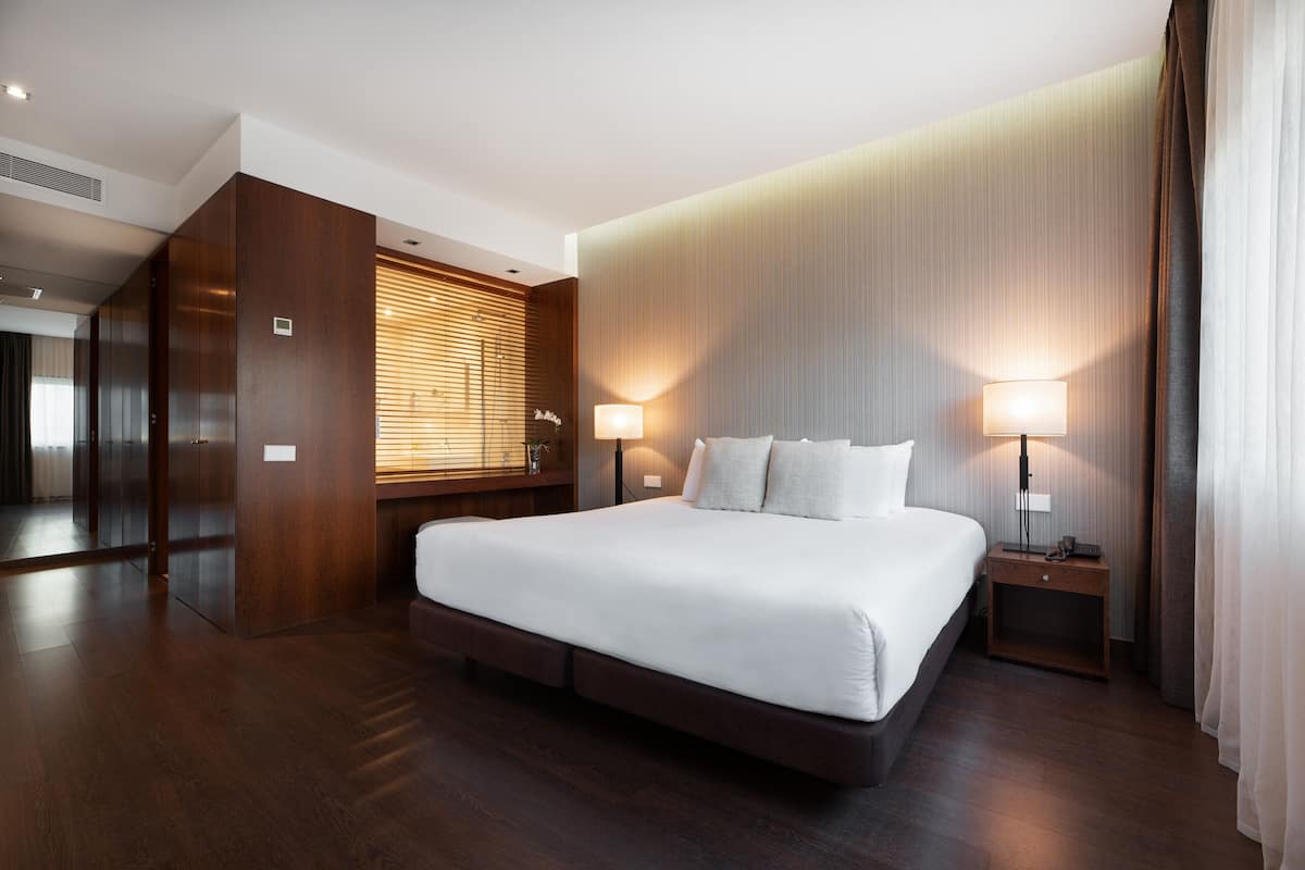 A modern hotel room with a large bed, wooden flooring, and a built-in wardrobe.