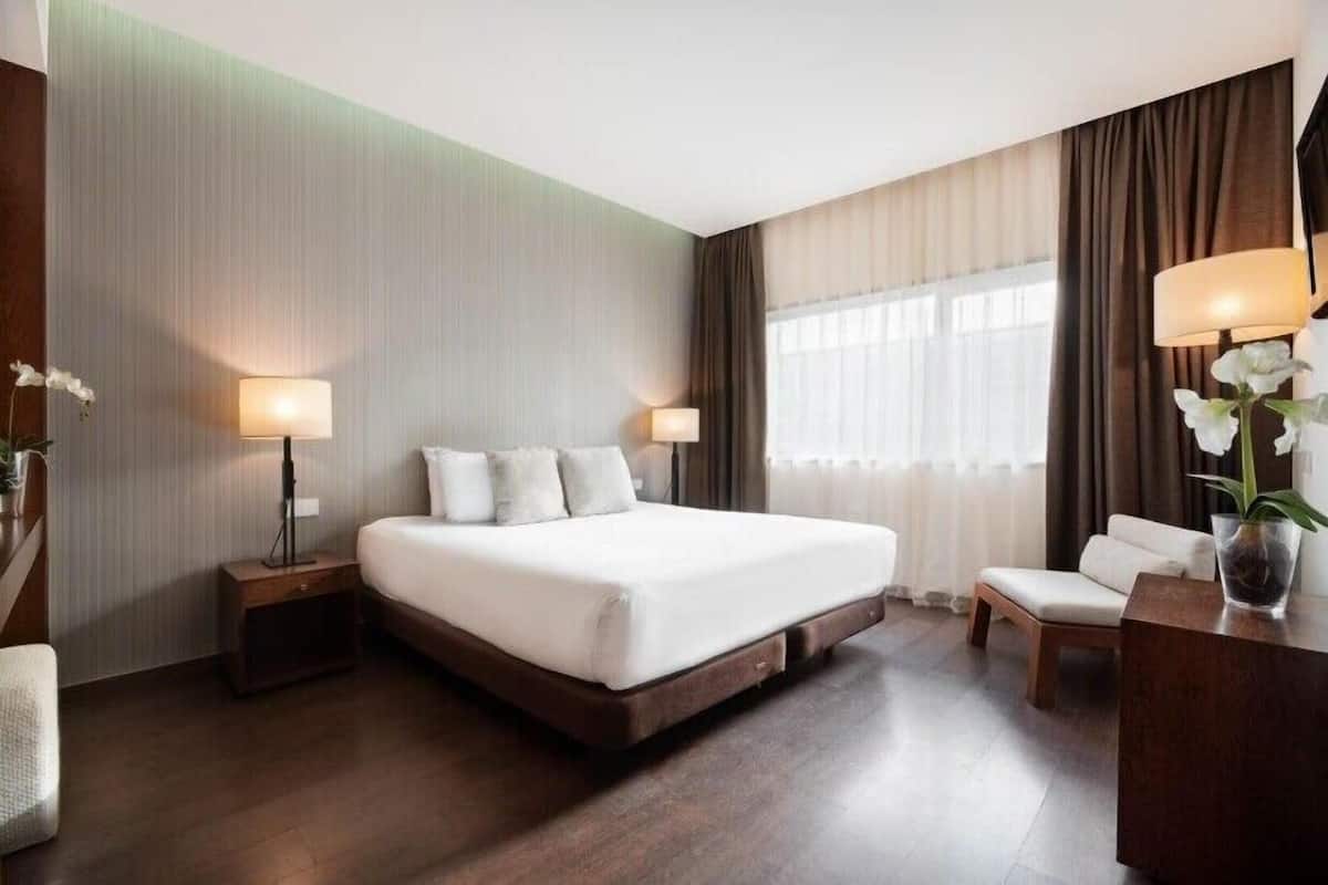 A hotel room with a large bed, bedside tables with lamps, a chair, and a desk with a lamp.