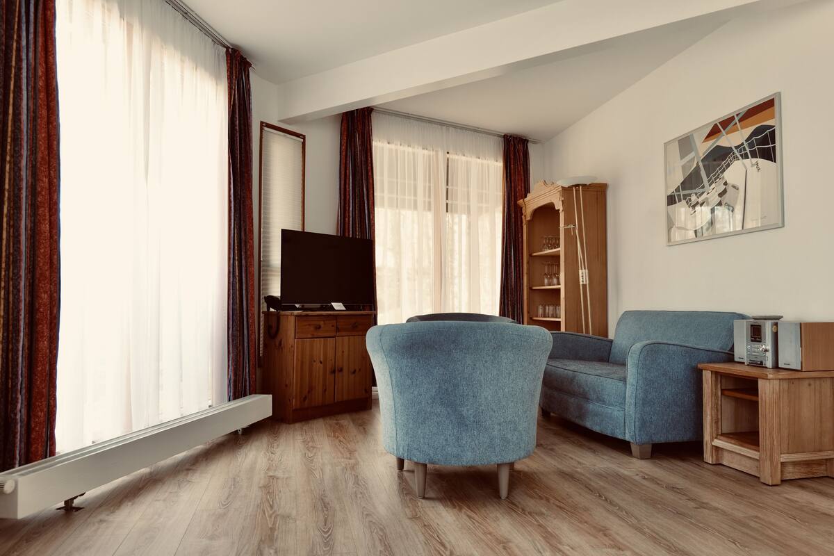 Ein Wohnzimmer mit Fernseher, blauem Sessel und einem Holzkabinett.