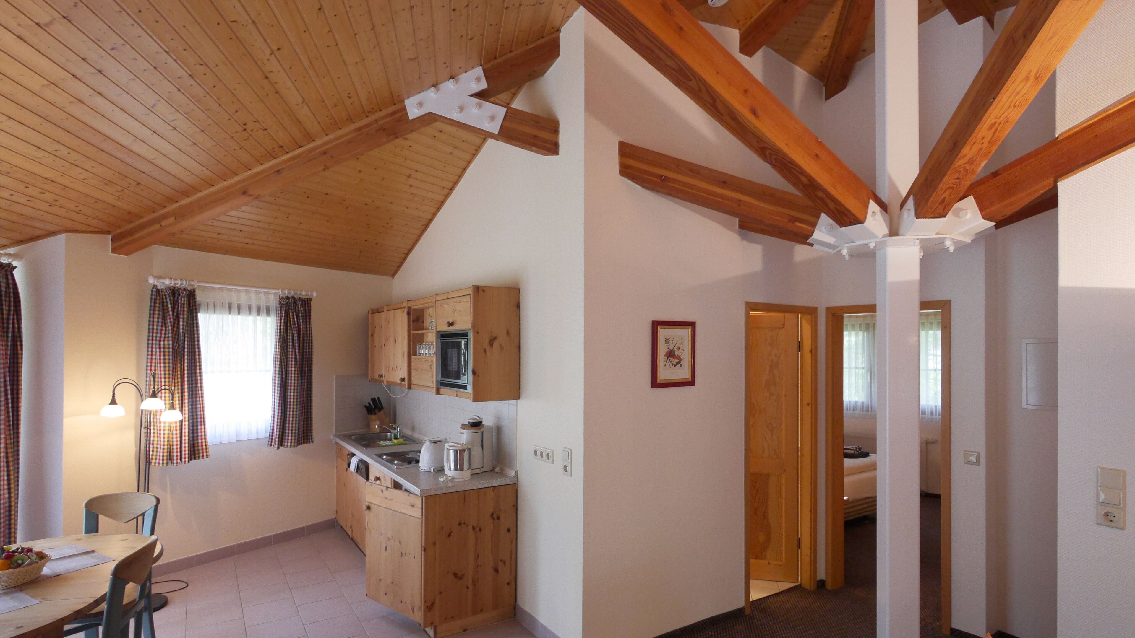 Una cocina con armarios de madera, una mesa de comedor con sillas y una ventana con cortinas.