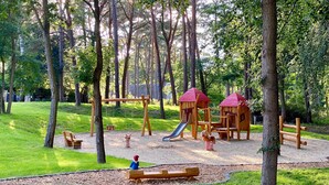 Un parque infantil con columpios, tobogán y estructuras para escalar, rodeado de árboles.