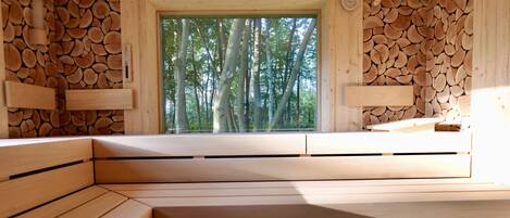 A wooden interior with a window view of trees, built-in benches, and a wall covered with logs.