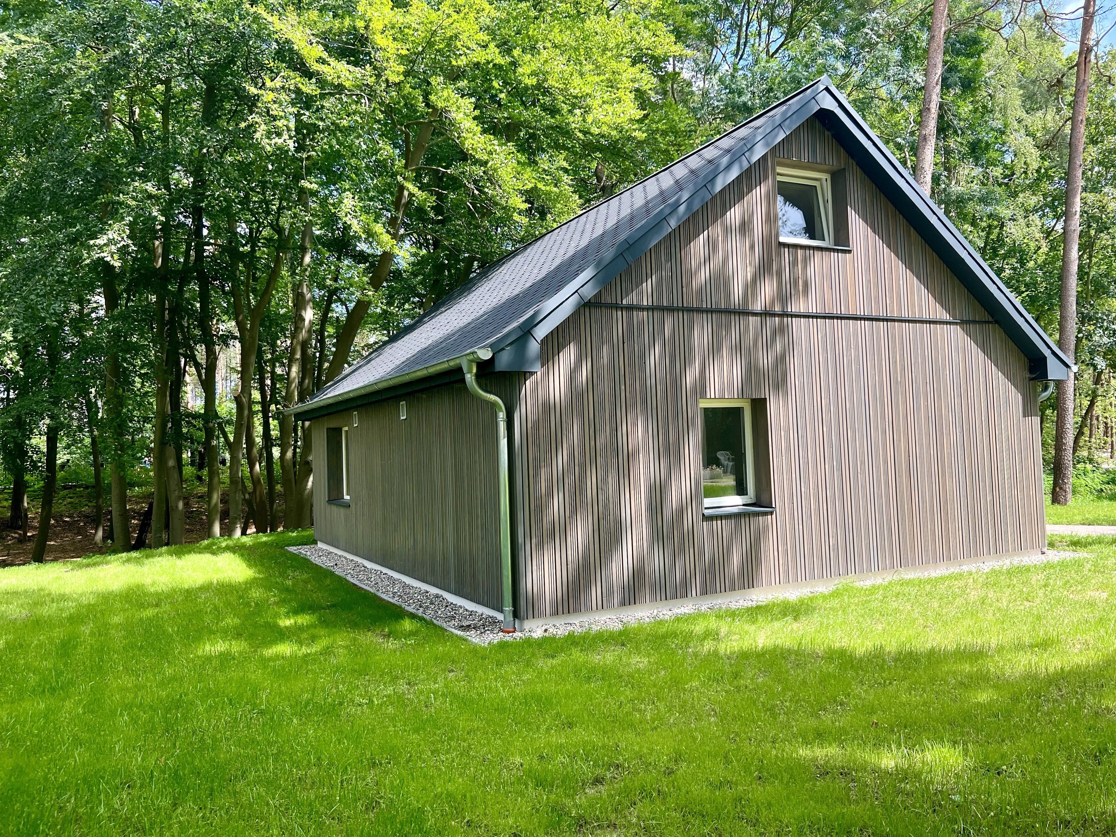 Eine Holzhütte mit geneigtem Dach, umgeben von einer Wiese und Bäumen.