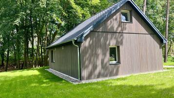 Eine Holzhütte mit geneigtem Dach, umgeben von einer Wiese und Bäumen.