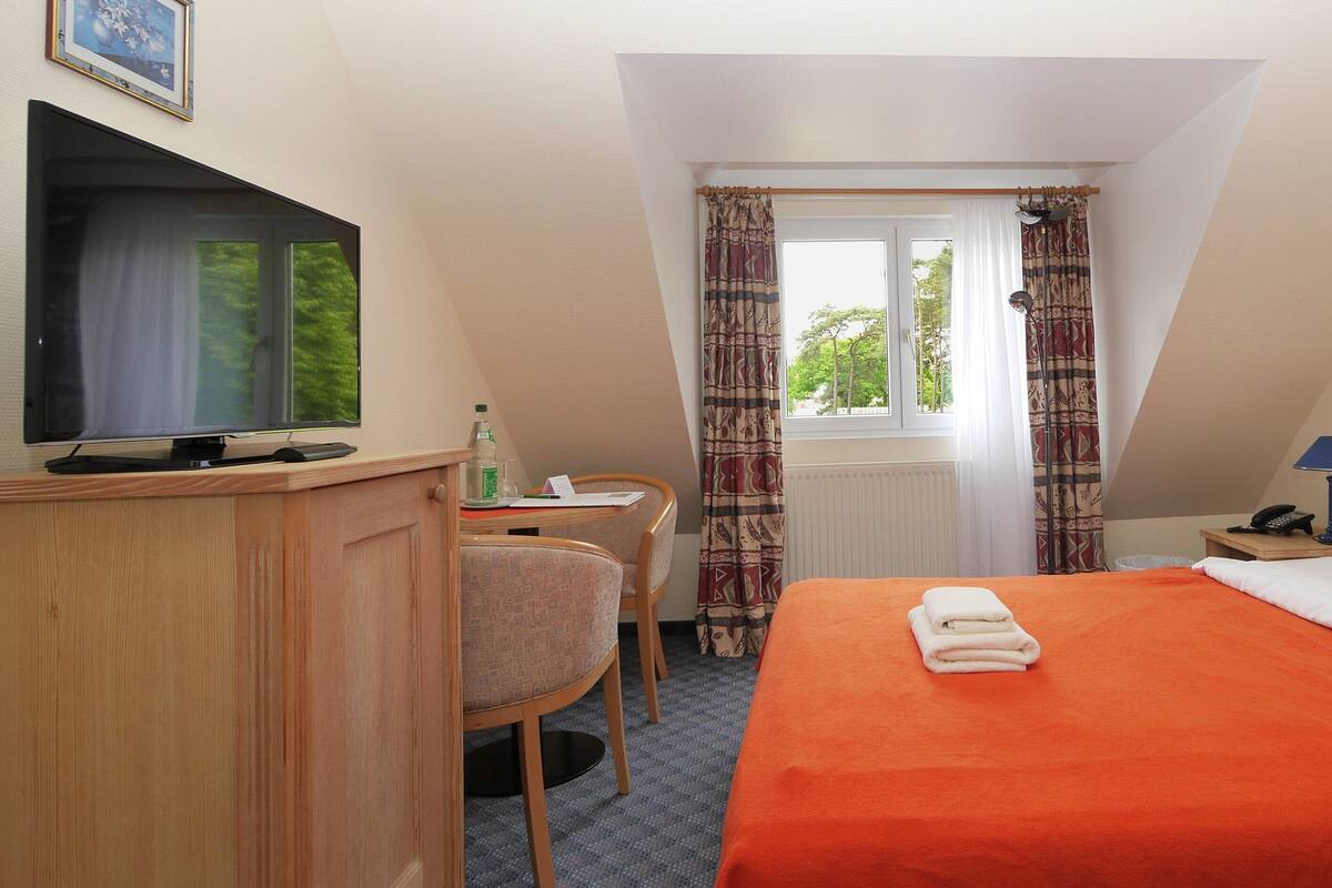 Ein Hotelzimmer mit Bett, Schreibtisch, Stuhl, Fernseher und einem Fenster mit Vorhängen.