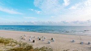 Una playa con hileras de sillas y sombrillas numeradas, orilla arenosa y el océano al fondo.
