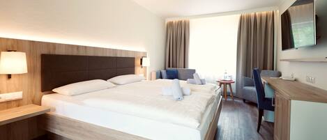 A hotel room with a large bed, a desk, a chair, a TV, and a window with curtains.