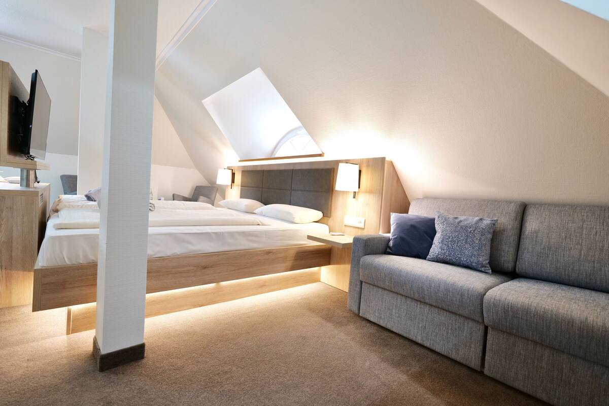 Ein modernes Schlafzimmer mit schrägem Dach, einem Bett, einer Couch und einem Schreibtisch.