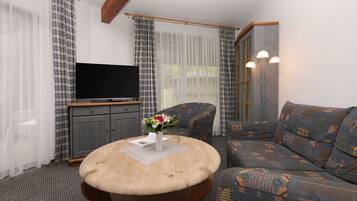 Una sala de estar con televisor, un sofá, una mesa de centro con un florero y cortinas.