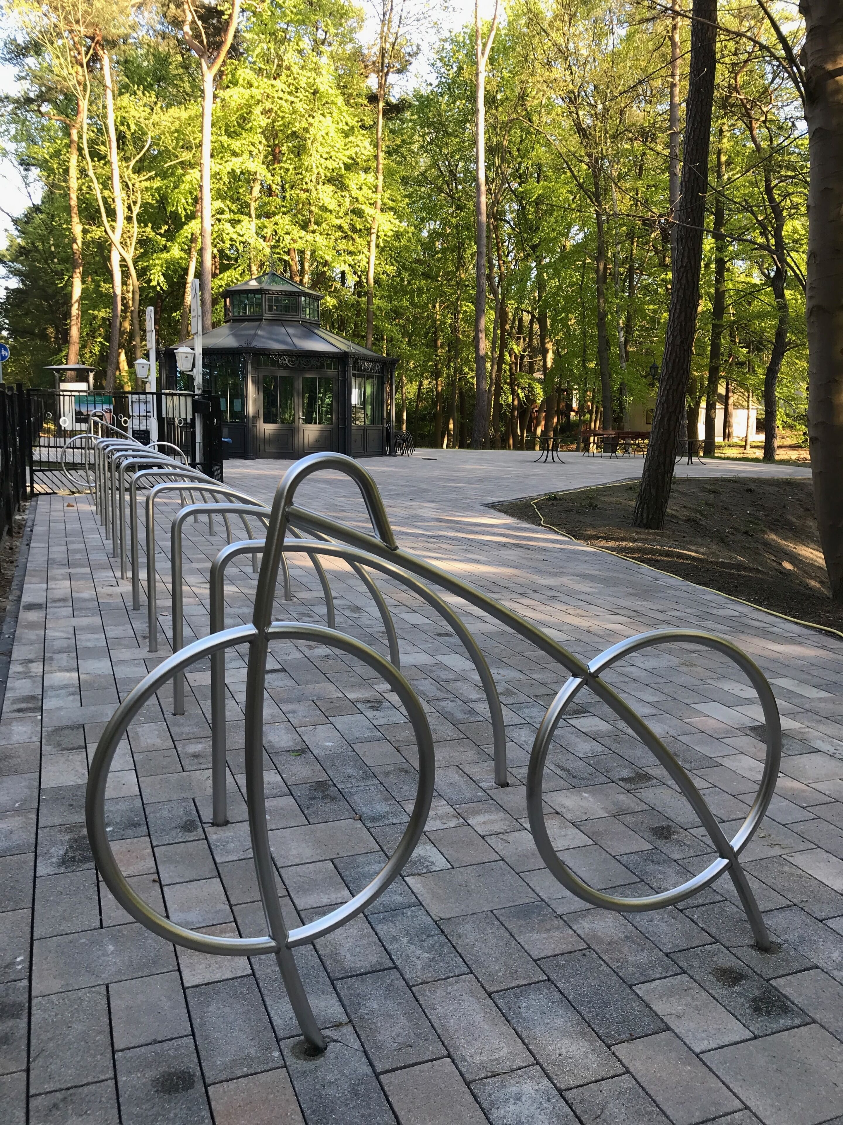 A paved walkway with metal bike racks and a gazebo in a park.