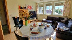 A dining area with a round table set for two, a sofa, and a TV in the background. - Ferienwohnung Fricke (Dresden)