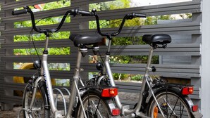 Two bicycles parked under a covered area with a metal structure and greenery in the background. - Ferienwohnung Fricke (Dresden)