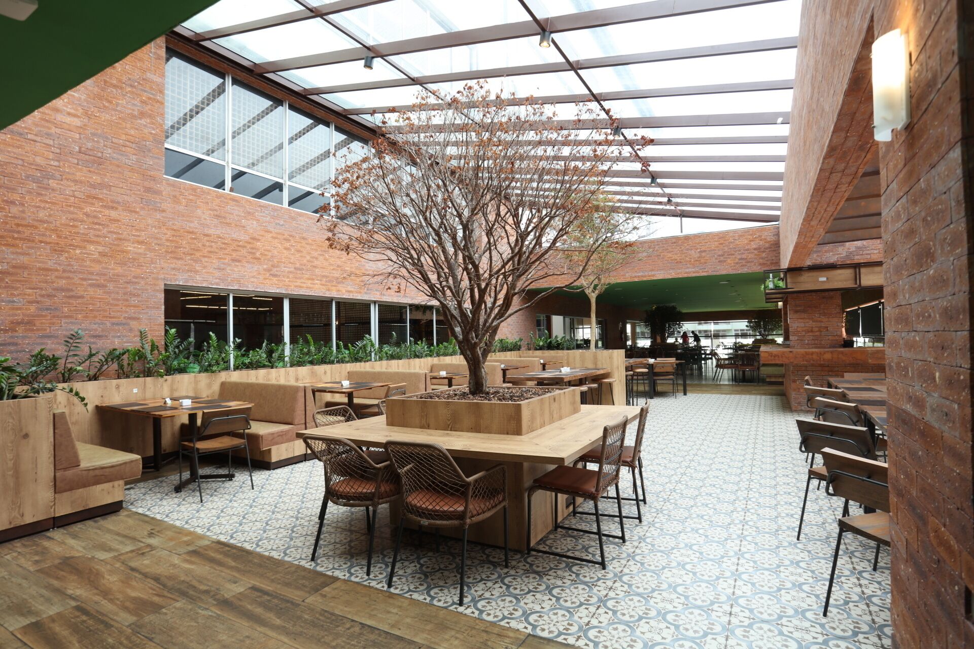 Un comedor interior con paredes de ladrillo, muebles de madera y un árbol grande.