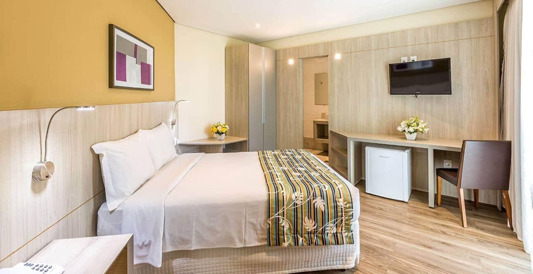 A hotel room with a bed, a desk, a television, and a small refrigerator.