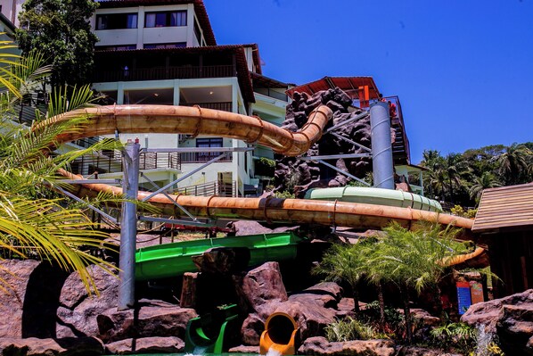 A water park with a large water slide, rock formations, and a building in the background.