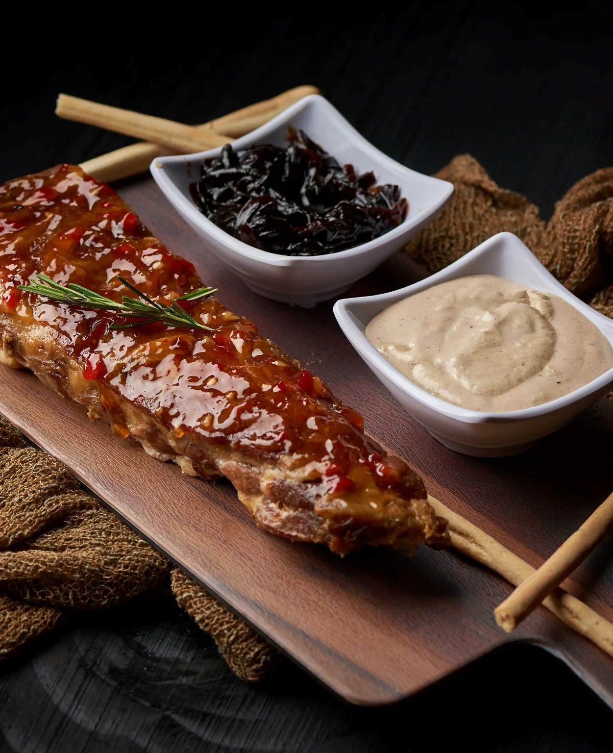 A charcuterie board with a glazed meat dish, pickled vegetables, and two types of dips.