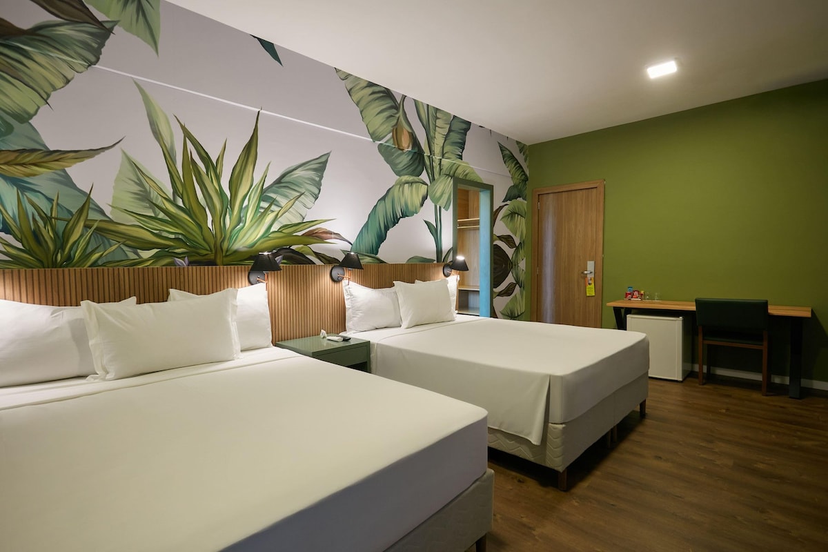 A hotel room with two beds, a wooden headboard, a green wall, and a large plant mural.