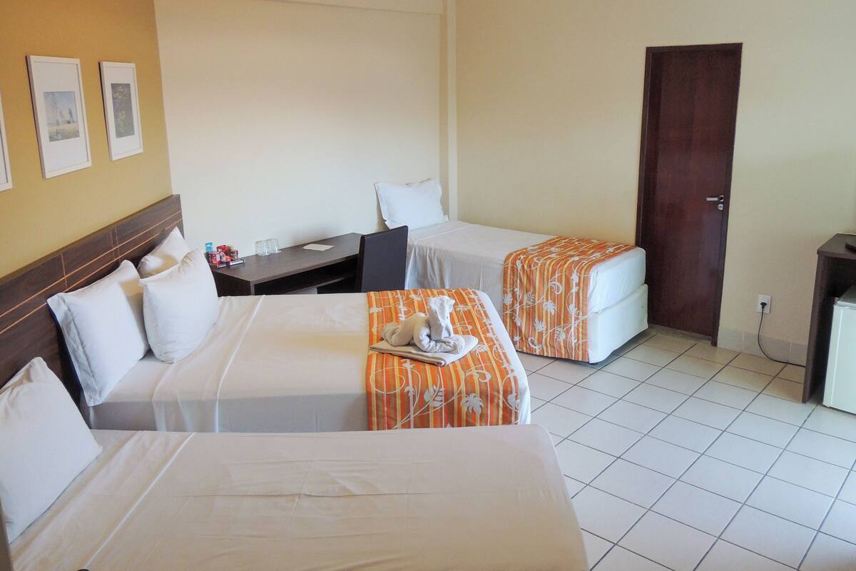 A hotel room with two beds, a desk, a chair, and a door.