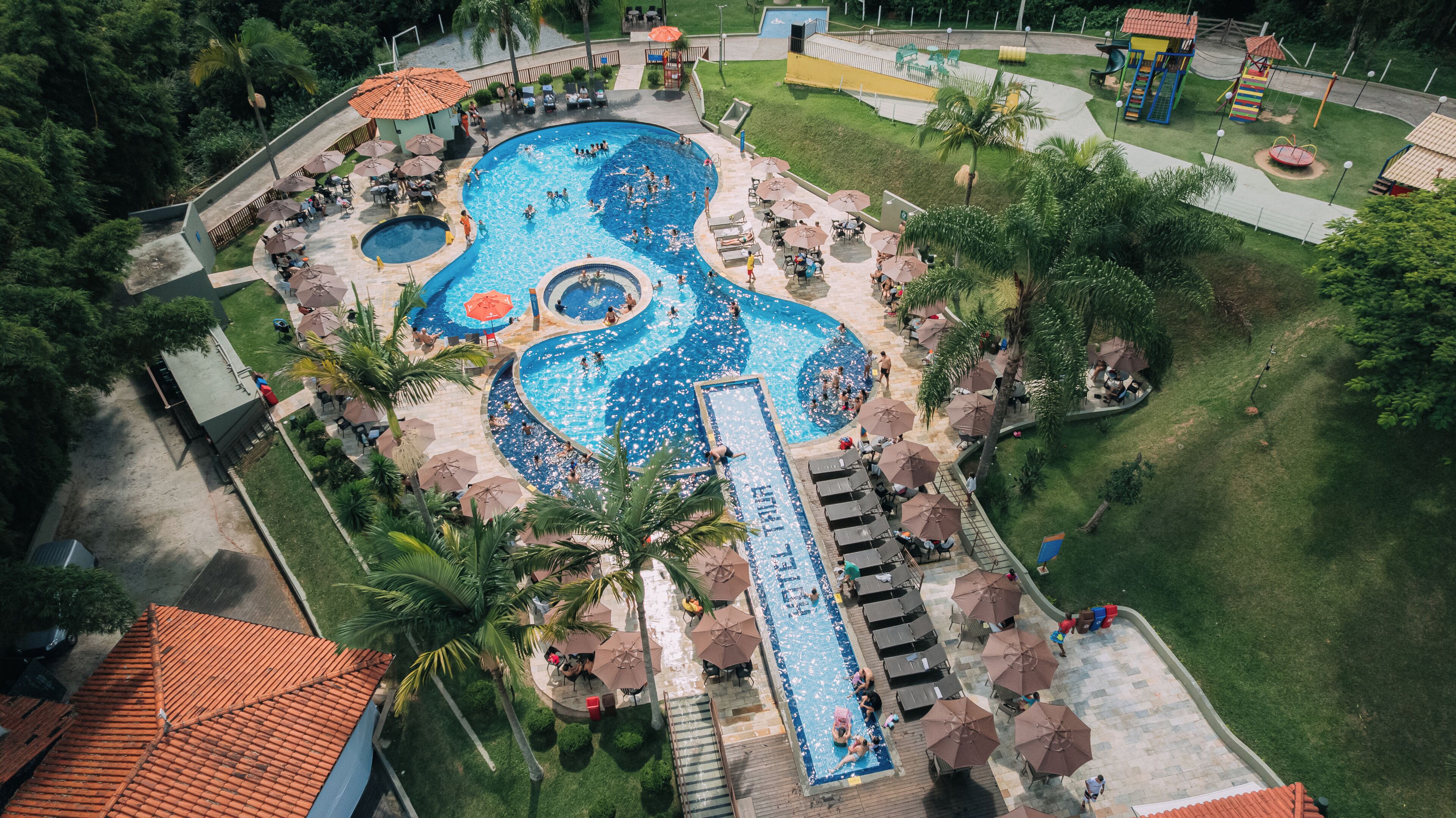 Vista aérea de um complexo de piscinas com várias piscinas, espreguiçadeiras e guarda-sóis.